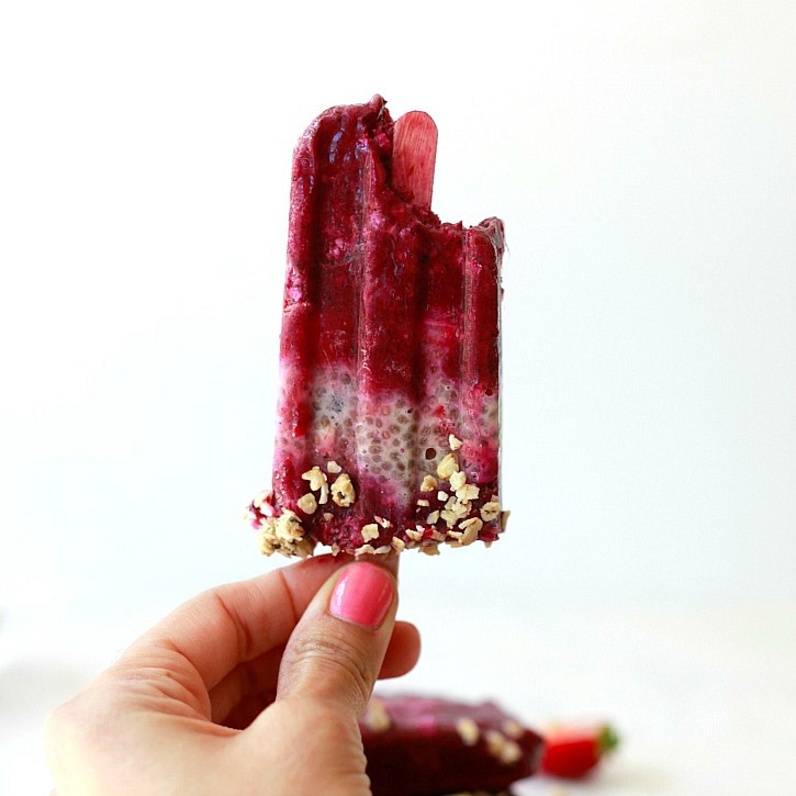 Acai, chia, and granola breakfast ice pops. Hand holding a purple acai, chia, and granola popsicle with a bite out of it.