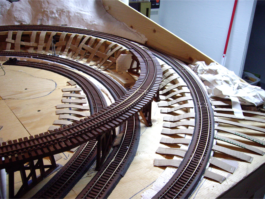 Cardboard strips being installed to the sides of a track grades and benchwork to form the base for hard shell terrain