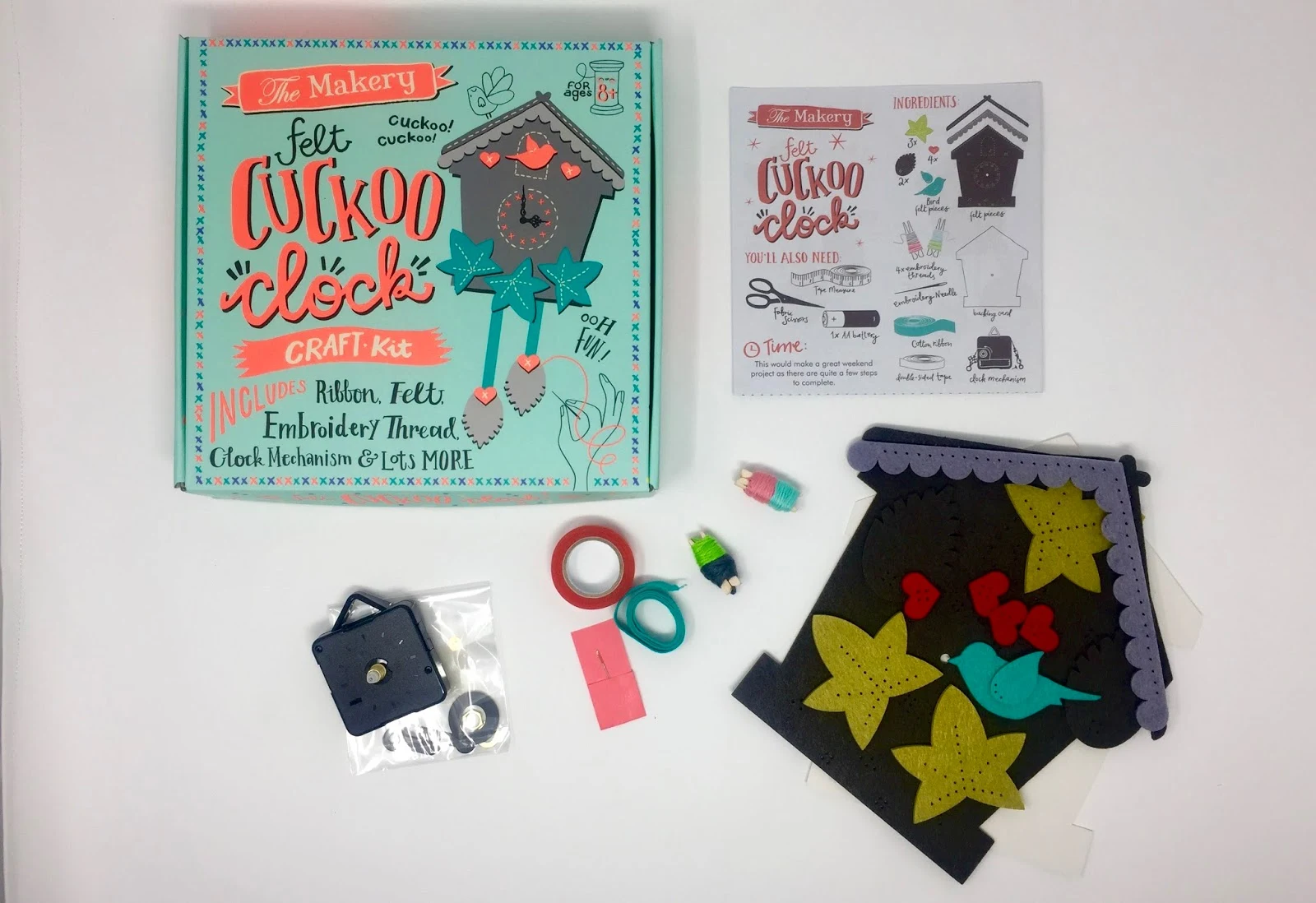 The Makery Felt Cuckoo Clock Craft Kit box next to the contents including instructions, pre cut felt pieces, clock parts, cotton, ribbon and a needle