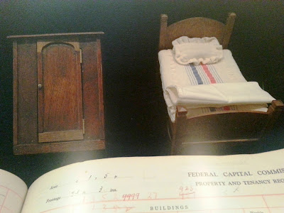 Vintage dolls' house 1930s wardrobe and single bed with bedding, in a display cabinet in a museum gallery.