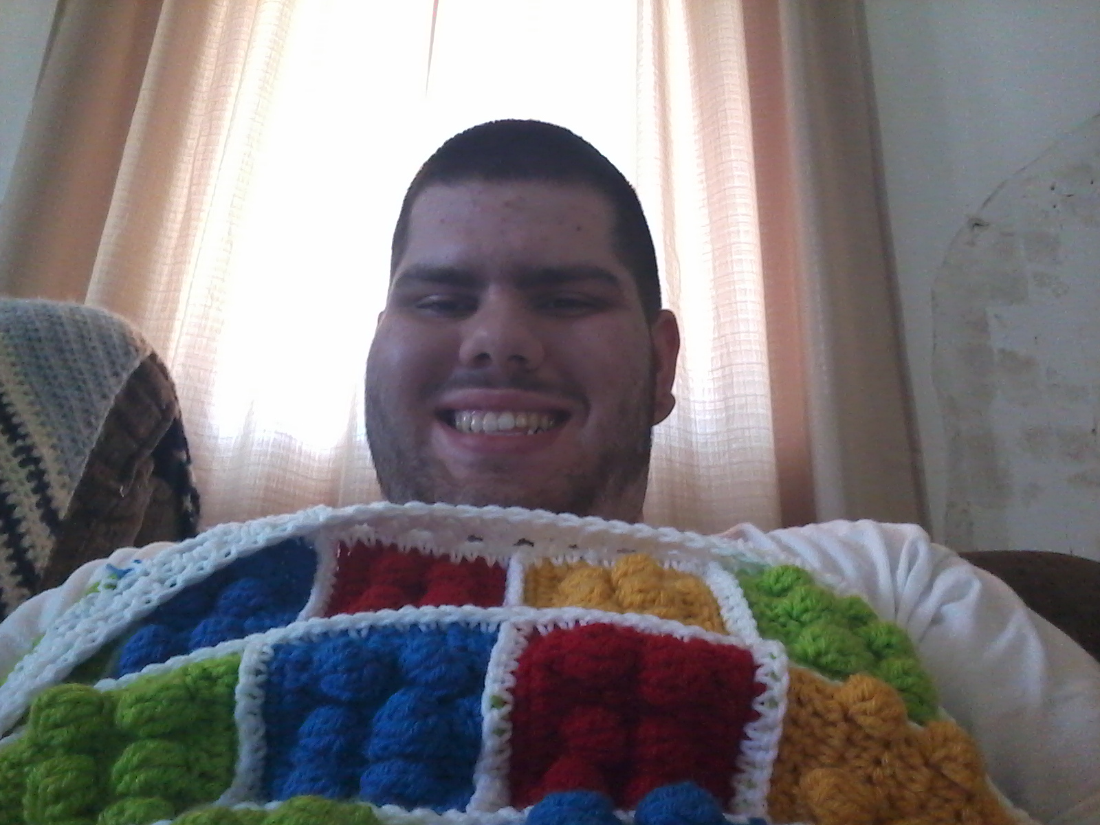 Teen smiling under a LEGO-inspired crochet blanket while building LEGO bricks