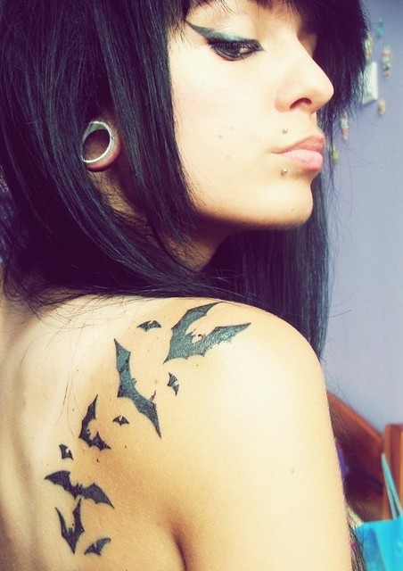 Chica morena de pelo largo, lleva tatuajes de murcielagos en el omóplato