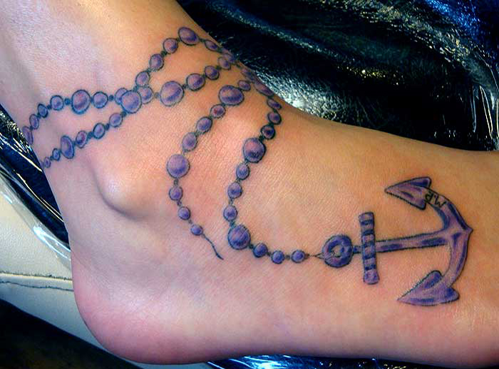vemos el pie de una mujer y su tatuaje recien terminado, el tatuaje de un ancla con rosario