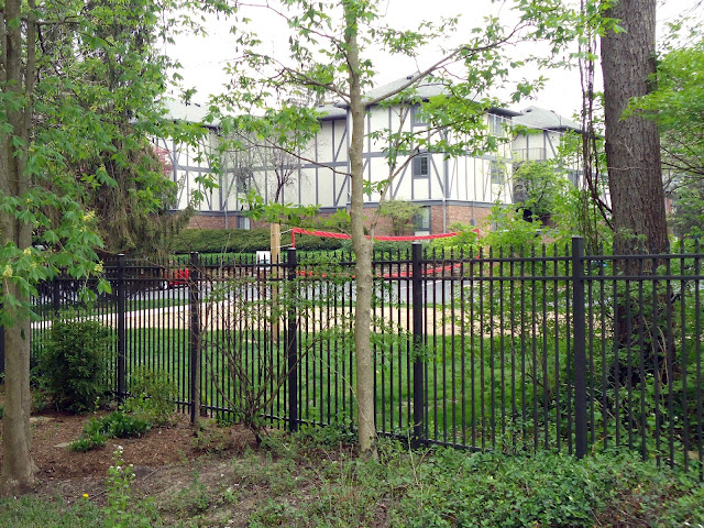 Large tudor-style apartment building amid trees, behind wrought-iron fence.