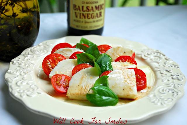 Caprese Salad made of tomato, mozzarella cheese, and basil with balsamic vinegar over it on a white plate with balsamic vinegar in the background