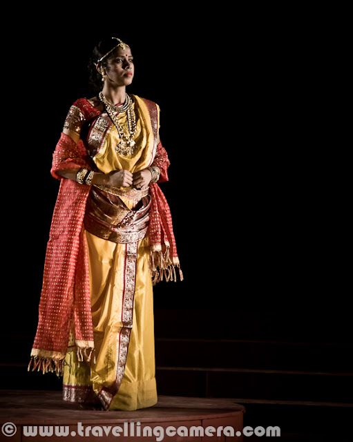 Here are some more pictures from the play Chandalika. To give you some context of the play, it was written by the legendary Rabindranath Tagore and it is the tale of Prakriti, an untouchable girl forced to live on the periphery of society as ‘chandalika’. No one want to play with her, people keep distance from her but at times interact with her for their personal benefits. The play is based on a story from a Buddhist text. Play starts with some dialogs by Usha Ganguli where she describes the situation of her region without water and how people are crying for water. Usha is playing main role in this play. She has a daughter and both of them are treated badly by higher society. At the same time, she helps the local kingdom by helping in various problems like water scarcity. Setting and expressions are two powerful tools used to assist dialogs and action in drama for conveying important information to the viewers. Through these tools a lot can be shown without actually being said. For example, firewood, earthen pots etc. show a rural setting and may also indicate that the play is set in past. Everything cannot be expressed in words because then  the play will be much too lengthy, boring and unintelligent.Interactions between characters, their expressions and their actions often hide a subtext that is very interesting to unearth. For example, in this scene, can you make out what the character is feeling of thinking without actually knowing what is going on? One can easily assume that the character is not unhappy and may even be pleased about things. I can also see a hint of dreaminess in the eyes and may be lost in thoughts about her beloved. But then that is my interpretation and how close it is to the actual emotions being portrayed by the character depends upon the character's acting skills and my ability to read expressions. The expressions here are more of defiance and questioning. But then again that is my interpretation and I can be wrong. Another thing you'd want to note is the attire and the make-up. All efforts are made to keep them true to the situation, the period, and the story. For example, here the dhotis and the lathis indicate that the setting is rural and the expressions of various characters indicate their emotions. For example, the person who is chained is reluctant to go where he is being led and the person in the red dhoti seems to be pleased with himself and takes pleasure in the predicament the chained person is in. Flowers, dances, audience, claps indicate celebrations of either a festival or an event. Some people are wearing garlands and this may indicate their special place in the society. Graceful dance moves and melodious singing are all often a part of dramas and I am amazed by the number of talents most of the stage artists hide within themselves. Almost all of them sing well and dance well along with obviously acting well. One-on-one interactions are some of the most interesting interactions in a play. They reveal more about a character and her relationships with other characters than any other interaction in a play. These are usually more difficult to carry out because the audience is focussed upon the characters involved. These are more challenging for the actors than for the directors.Multiple characters interactions are more challenging for the playwriter and for the director because it requires exceptional skills to craft such scenes. Colors and body languages tell stories of themselves. The next time you go to watch a play, try to keep an eye on these things and you will be amazed at what you will discover.Presence of objects such as cages can be symbolism that you had never suspected. If you observe these things, you will add layers to your play-watching experience. For example, here it is clear that the woman in the centre is someone who has power over the other two. The cage represents imprisonment or curtailment of freedom. The attire of this woman indicates affluence and her demeaner indicates power and even royalty. Is there anything else you can make out? Feel free to leave a comment if you can. The body language of the characters here indicates a mother-daughter relationship. And the leaves and the leaves indicate some sort of a ritual or religious practice. The clothes of these two characters are much simpler. The characters are not affluent but aren't poor either. Let me know if you can read more into these pictures. I would love to know. Please feel free to leave a comment.