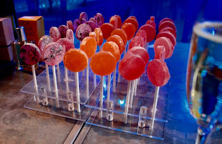 Yellow, orange and red lollipops on wooden thin cylindrical sticks on a rectangular silver box on a silver rectangular table with a blue cloth on a dark background 