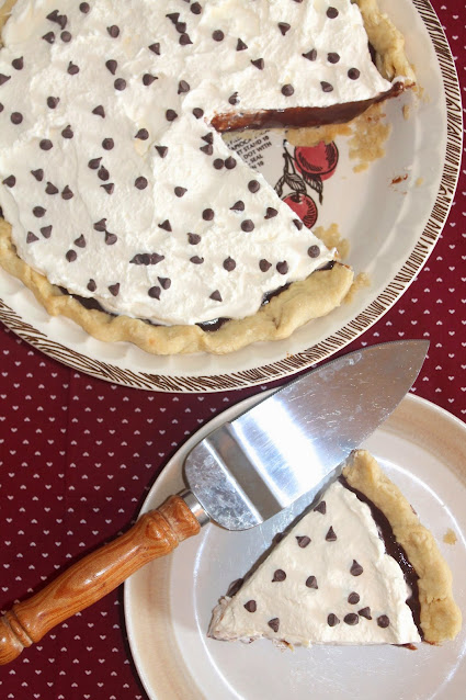 View of finished chocolate cream pie with a pie cut out and sitting on a small plate.
