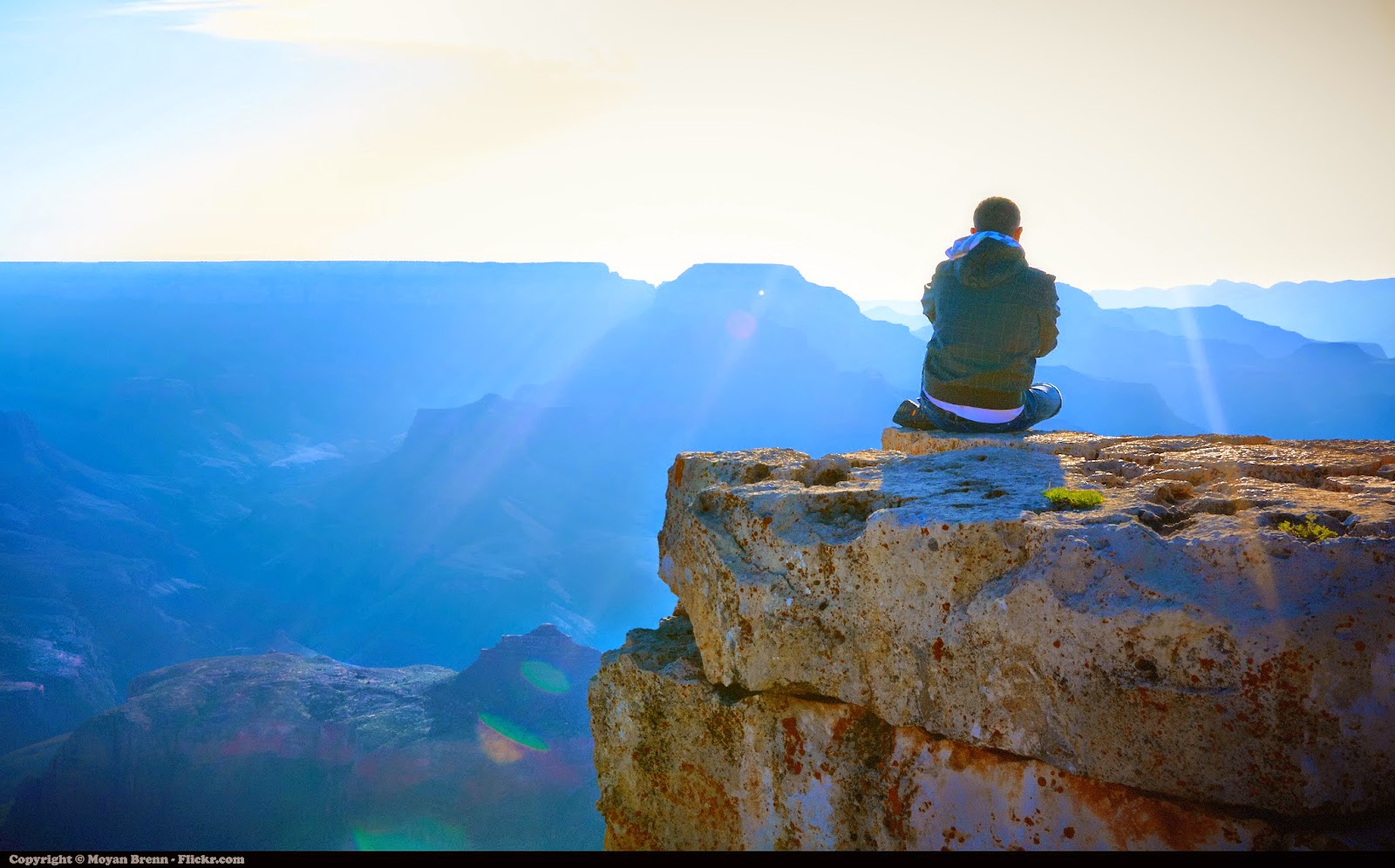 Meditation by Moyan Brenn: Man sitting on mountain top, looking at sunrise over valley. 