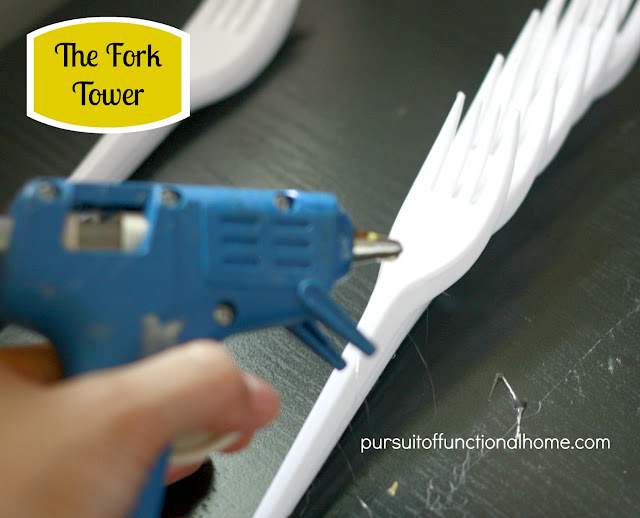 The Fork Tower Project. Blue Hot Glue Gun and white forks on top of the table. 