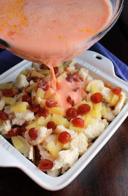 pouring pink custard over bread and fruit for tropical bread pudding