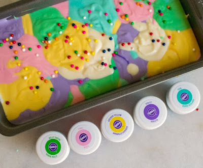 dollops of different colors of ice cream base in loaf pan with bottles of gel food coloring nearby