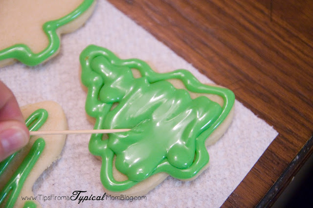 Using a toothpick to spread the royal icing around the cookie