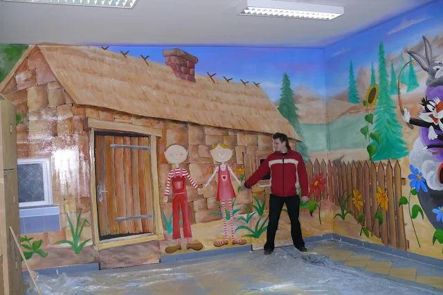 Artystyczne malowanie przedszkola, motyw bajkowy malowany na ścianie w szkolnym korytarzu.