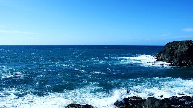 De zee en een strak blauwe lucht met rotsen