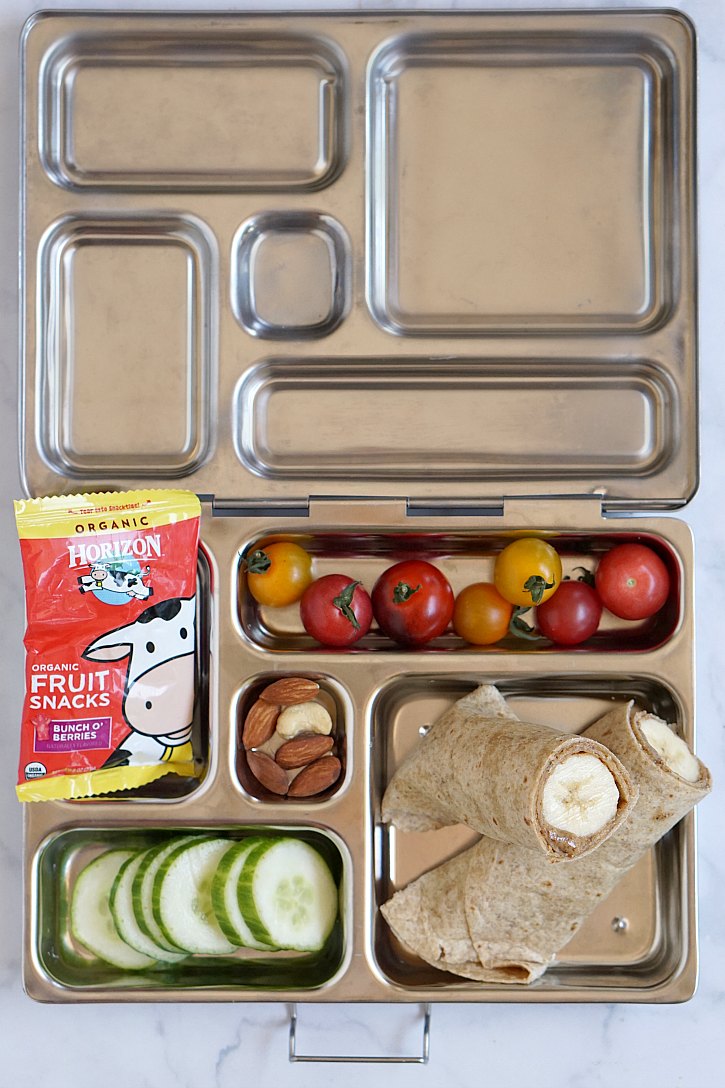 Kids lunch box idea with a banana nut butter wrap Vegetarian kids lunch box with banana almond butter tortilla wrap, fruit, veggies, nuts, and Horizon fruit snacks.