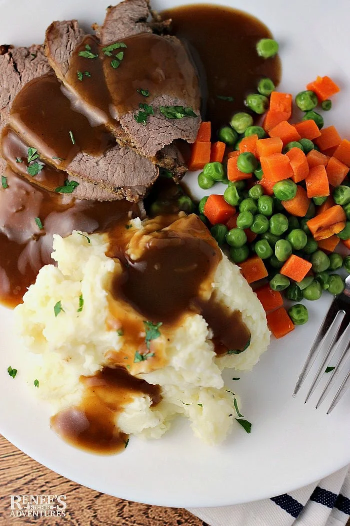 Garlic Parmesan Mashed Potatoes on plate with gravy, roast beef, and peas and carrots