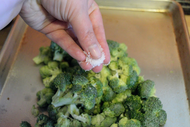 Broccoli florets on the baking sheet being seasoned with salt. 
