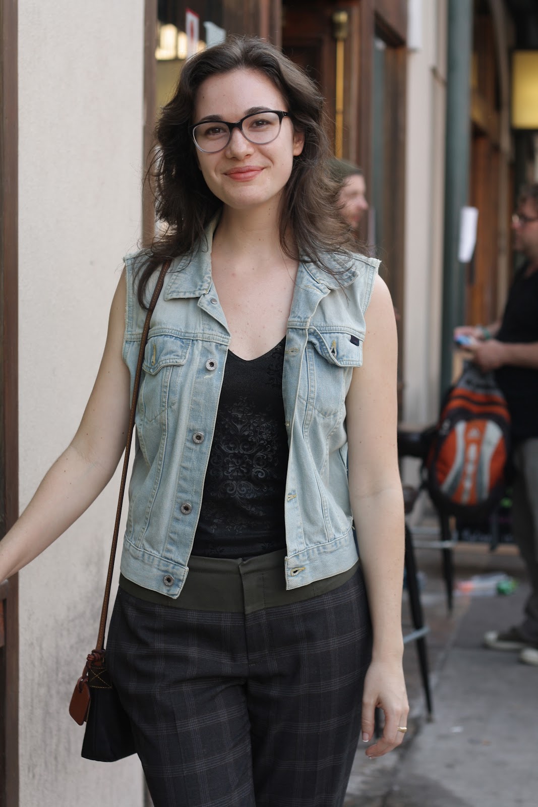 brunette girl wearing a denim vest, black tank, and glasses