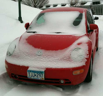 Red Volkswagen Beetle with a snow coating, leaving shapes like devil horns on the windshield