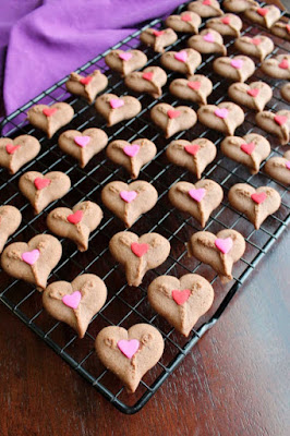 Cute chocolate cookies are just minutes away with the fun spritz cookies. Sandwich some ganache frosting between them for an extra delightful dessert treat! cooling rack full of chocolate spritz heart cookies with heart sprinkles