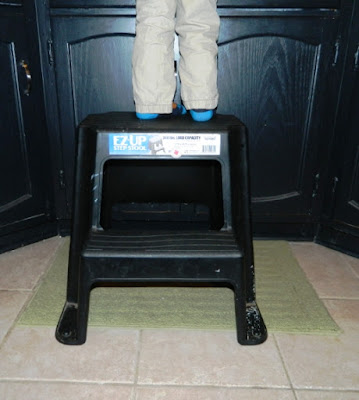 Photo of young boy's legs standing on a black plastic stool at the sink