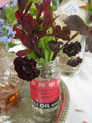 A dark double auricula and bright green meadowsweet arranged in an old chilli oil jar.