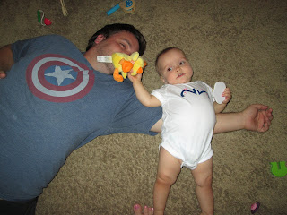 dad laying on floor with baby girl laying over his arm holding duck toy