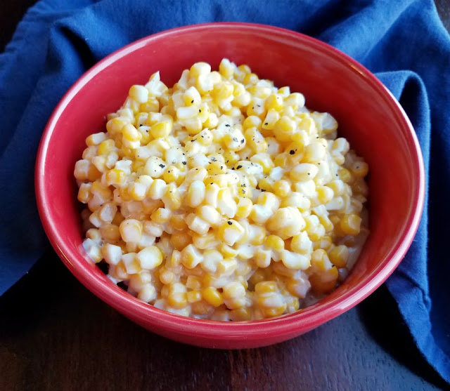 This corn is soooo good. It is creamy and easy and cooks in the slow cooker freeing you up to do other things! It is a perfect side dish for almost any dinner and one the family is sure to love! creamy corn in red bowl with sprinkling of black pepper on top