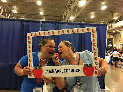 two woman pose with a Apple Crunch frame and an apple