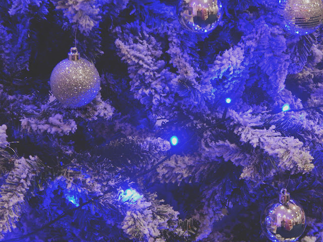 Blue Christmas tree with snow and ornaments hanging from it.