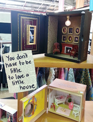 Dolls' house room boxes on a market stall next to a sign which says 'You don't have to be little to love a little house'