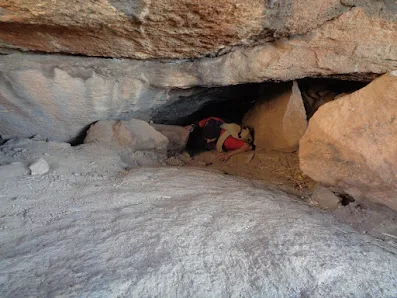 Hiker squeezing through a small cave entrance at Kunti Betta