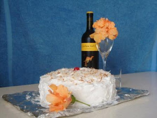 A white frosted cake with a bottle of red wine on a table.