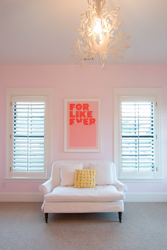 Nursery with pale pink walls, simple art, a white love seat, and modern tole chandelier