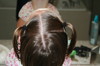 Back view of young girl's hair being styled into "Two Messy Twists on Top" Hairstyle