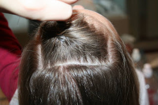 Top view of young girl's hair being styled into "Hair Twists into Messy Buns" hairstyle 