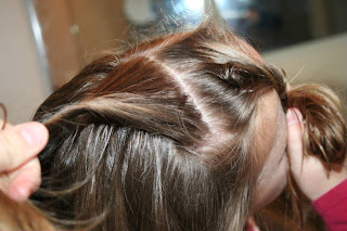 Top view of young girl's hair being styled into "Hair Twists into Messy Buns" hairstyle 