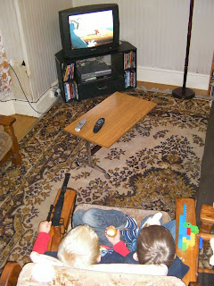 2 men, 1 chair. watching TV in parallel