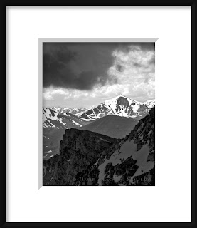 A black and white photo of the rugged Rocky Mountains of Colorado rise up to touch the storm clouds creating matching angles.