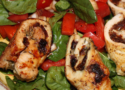 cooked pesto chicken rolls on top of tomato and spinach salad