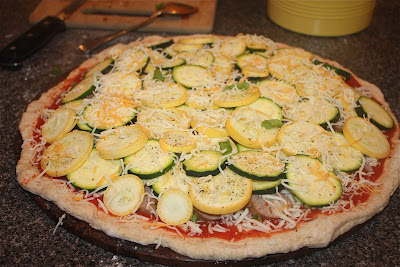 uncooked pizza dough topped with tomato sauce, cheese, sausage, zucchini, and squash