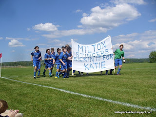The Milton Stingers boys soccer team running with a Kickin it for Katie banner