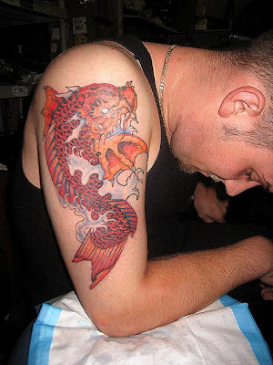 Red koi tattoo in the splashing water on a white boy upper arm.