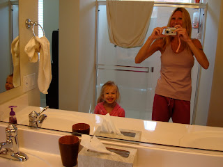 Young girl and woman smiling into mirror in bathroom