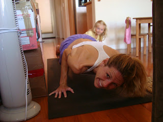 Woman with little girl in background doing chaturunga dandasana yoga pose