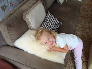 Smiling little girl cuddling fuzzy pillow on brown couch