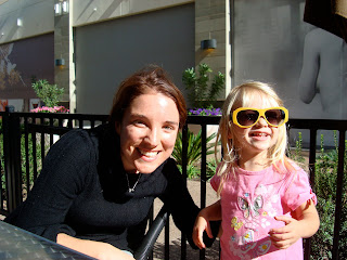 Woman with arm around young girl smiling wearing large yellow sun glasses