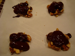 Four piles of pecans topped with melted chocolate on parchment paper