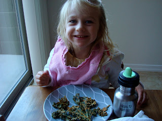 Young girl sitting at table eating a plate full of Kale Chips